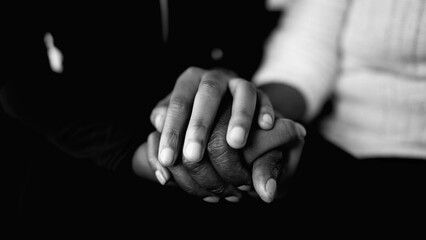 Caring for the eldrly - close-up detail of holding hands in dramatic black and white. Younger hand...