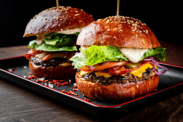 Two gourmet burgers with fresh toppings on a black plate, highlighted by dramatic lighting