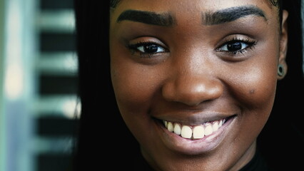 One happy young black teen girl smiling at camera in detail macro close-up, looking directly at...