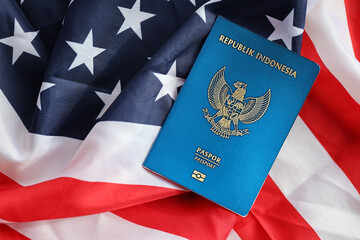 Fototapeta premium Blue Republic Indonesia passport on United States national flag background close up. Tourism and diplomacy concept