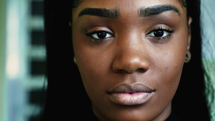 Macro close-up portrait of a serious young black woman looking directly at camera with solemn...