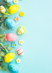 Easter background or greeting card on blue. Eggs, spring leaves, flowers and colored butterflies. Flat lay with copy space.