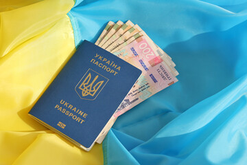 One Ukrainian biometrical passport and UAH hryvnia bills on folded waving flag of Ukraine country...