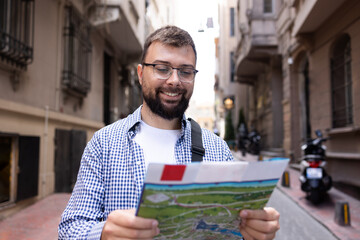 Optimistic smiling with white teeth young bearded man in glasses and casual clothes reading paper...