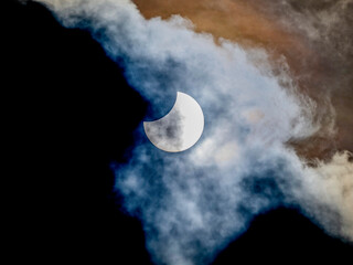 Partial solar eclipse peering through wispy clouds