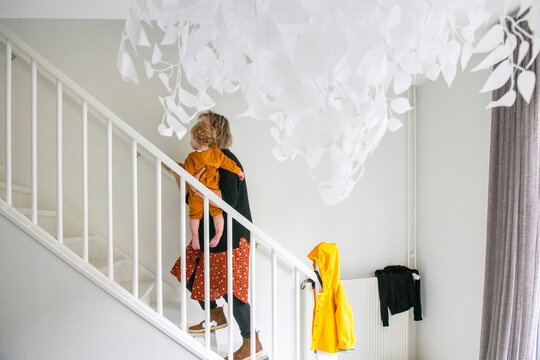 A child ascending a bright staircase, pausing to look upwards at a whimsical hanging decoration.