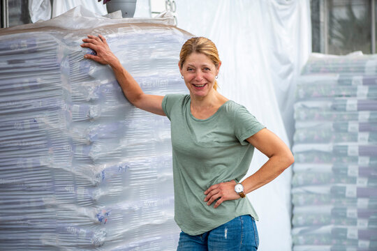 Woman smiling in a warehouse environment with stacked products.
