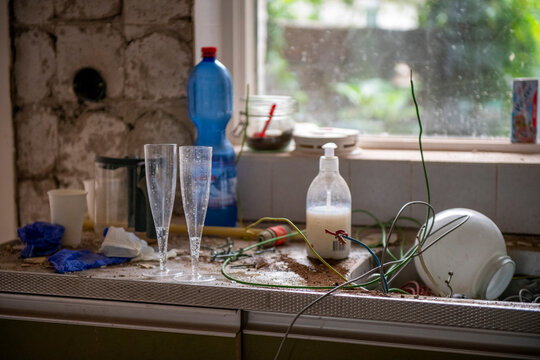 A chaotic kitchen windowsill with a cluttered assortment of items.