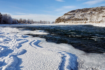 A frozen river bank with a distant mountain under a cloudy sky