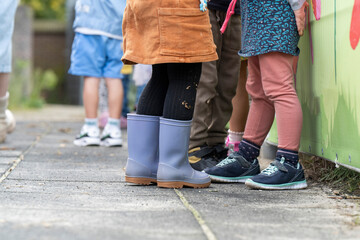 Children lined up against a colorful fence, showcasing a variety of footwear and playful attire.