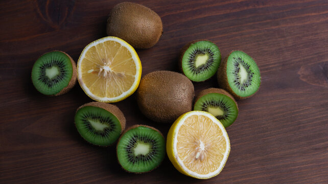 This captivating image showcases a delightful arrangement of fresh kiwis and lemons on a dark wooden surface