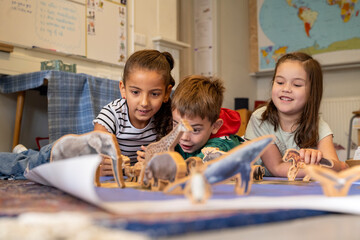 Three kids fascinated by dinosaur toys and a book on the floor