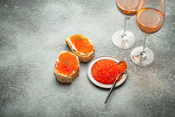 Small metal plate with red salmon caviar, two caviar toasts canape, two glasses of champagne top view on grey concrete background, festive luxury delicacy and appetizer. - 757235105