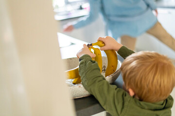 Little hands grabbing a banana from the kitchen counter.