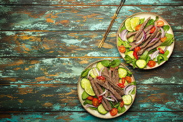 Two plates with traditional Thai beef salad with vegetables and mint top view served on rustic wooden background, healthy exotic asian meal, space for text. - 757235794