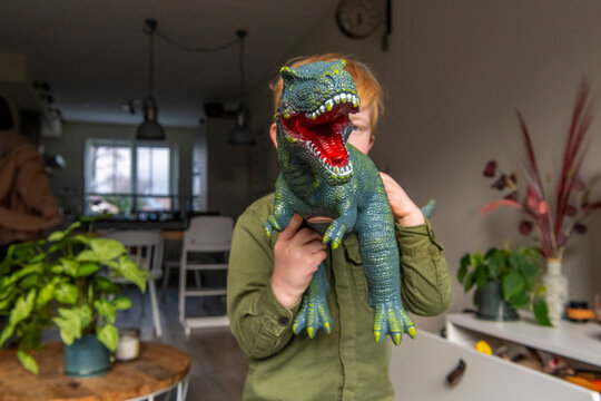 Child playfully poses with a toy dinosaur covering their face