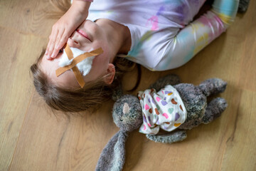A young girl lying on the floor resting with her plush bunny by her side, both looking like they're in need of some TLC.