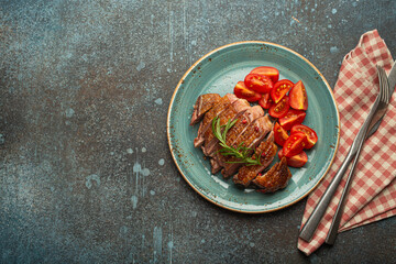 Delicious roasted sliced duck breast fillet with golden crispy skin, with pepper and rosemary, top view ceramic blue plate served with cherry tomatoes salad, concrete rustic background, copy space. - 757236329