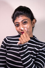 A woman with a black and white striped shirt is holding a cigarette in her hand. She has a red lipstick on and is making a funny face