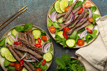 Two plates with traditional Thai beef salad with vegetables and mint top view served on rustic concrete background, healthy exotic asian meal. - 757237725