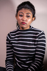 Fototapeta premium A woman with black and white stripes on her shirt is sitting on the floor. She has red lipstick on her lips and a serious expression on her face