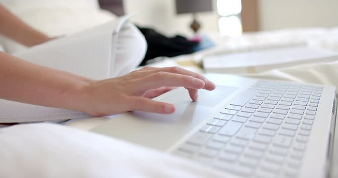 Close-up of a teenage girl's hands typing on a laptop with a notebook beside them at home