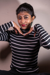 A woman is sitting on the floor and wearing a black and white striped shirt. She is smiling and making a peace sign with her hands