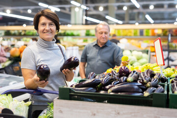 Elderly woman chooses eggplants in vegetable and fruit department