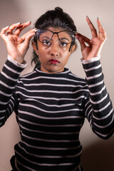 A woman wearing a striped shirt and glasses is holding her glasses up to her face. Concept of focus and attention to detail, as the woman is examining her glasses