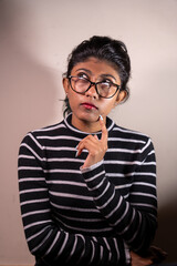 A woman with glasses is looking at the camera with a thoughtful expression. She is wearing a striped shirt and has her hands on her hips. Concept of contemplation and introspection