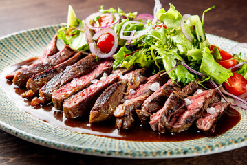 steak cooked to a medium-rare level and is garnished with salt flakes and herbs. Adjacent to the steak is a fresh salad consisting of green lettuce leaves, sliced onions, and halved cherry tomatoes.