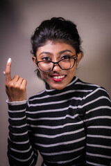 A woman with glasses is smiling and pointing her finger. She is wearing a striped sweater and has red lipstick on
