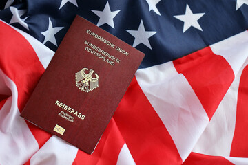 Red German passport of European Union on United States national flag background close up. Tourism...