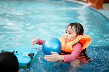 A little asian girl in swimming in the pool. Cute girl playing in outdoor swimming pool on a hot summer day. Kids learn to swim.