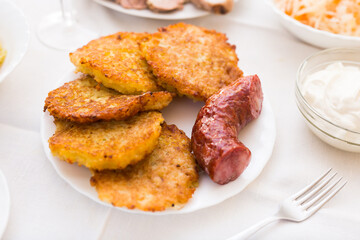 Fried grated potato pancakes with fried sausage on white plate