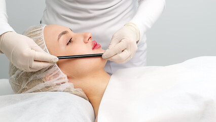 A master performs a lip augmentation procedure on a woman in a beauty salon in a beauty salon. Before the procedure, he makes corrections with a marker. Concept of cosmetology, surgery and injections.