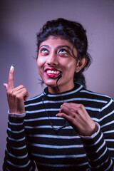 A woman with a black and white striped shirt is smiling and pointing her finger. She is wearing glasses and has a red lip. Concept of playfulness and confidence