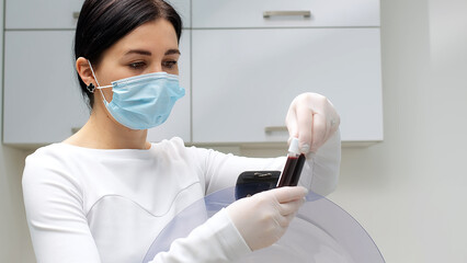 A cosmetologist in a white coat and gloves checks and demonstrates a blood collection tube with...