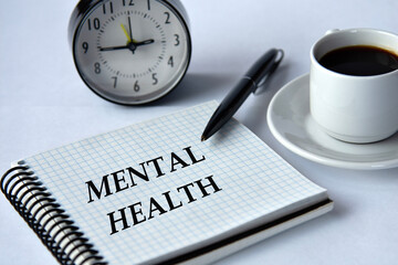 MENTAL HEALTH - words in a notebook on a white background with a clock and a cup of coffee