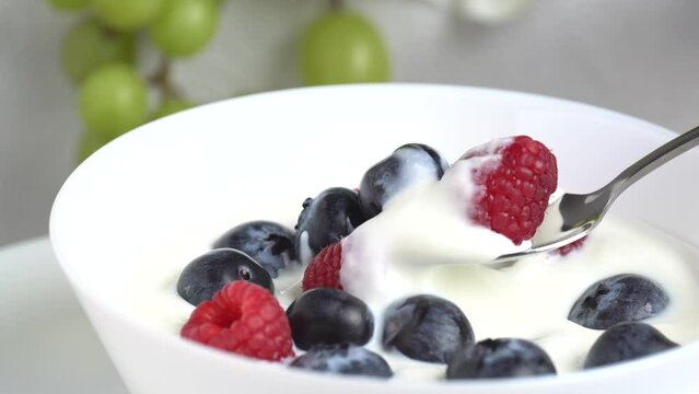 Greek yogurt with raspberry and blueberry scooped withs poon from a bowl, close up