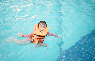 A little asian girl in swimming in the pool. Cute girl playing in outdoor swimming pool on a hot summer day. Kids learn to swim.