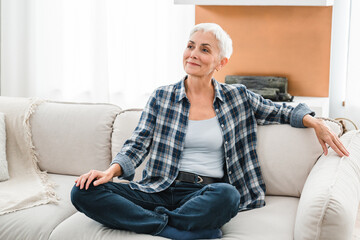 Dreaming mature woman sitting on the couch thinking about future at home. Caucasian middle-aged...