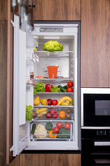 Open luxury refrigerator filled with lots of different types of food and drinks with a shelf full of fruits and vegetables.