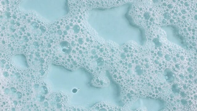 Bubbles of white soap foam on a blue background. Bathtup Soap Foam. Texture of Soap Foam Bubbles. Natural White Shampoo Bubbles Motion. High quality 4k footage