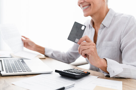 Cropped image of smiling businesswoman doing online shopping with credit card and laptop. Closeup photo of female employee paying remotely with debit plastic card