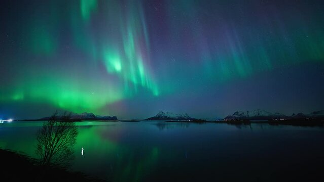 Panoramic view of the northern lights reflecting in a silent fjord in the beautiful mountainous landscapes of Steigen on March 3rd, 2024.