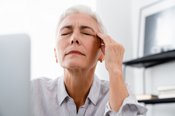 Businesswoman suffering from headache while working on laptop in office. Mature middle-aged manager...