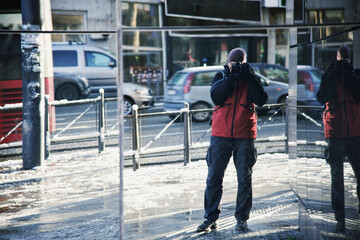 a man with a camera in his hands looks into a mirrored window in the city