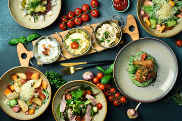 A set of food and dishes in plates. Top view. Food banner. On a dark stone background.