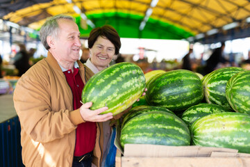 Elderly man and a woman buy a watermelon at an open air market